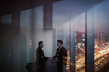 Poster Businessmen shaking hands in office at night