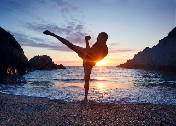 Canvas Print Man practising kung fu kick along beach at sunset