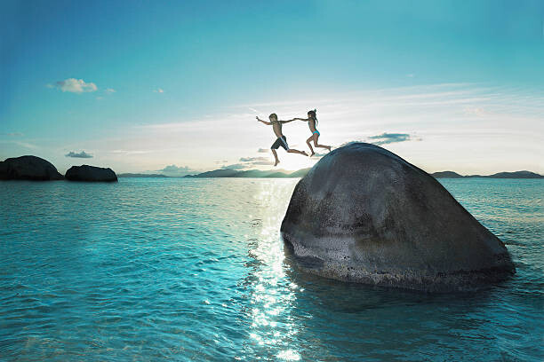 Juliste Two kids holding hands jumping off rock into sea