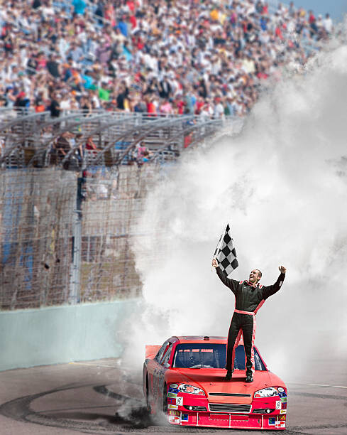 Juliste Winning driver standing on hood of race car.
