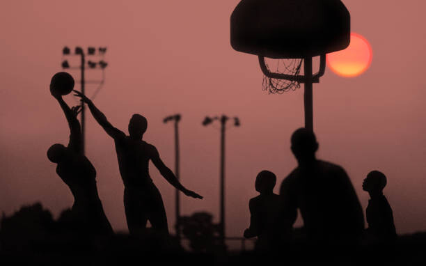 Slika na platnu Young men playing basketball at sunset.