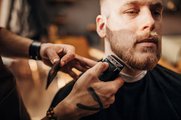 Poster Male barber cutting beard of client in barber shop