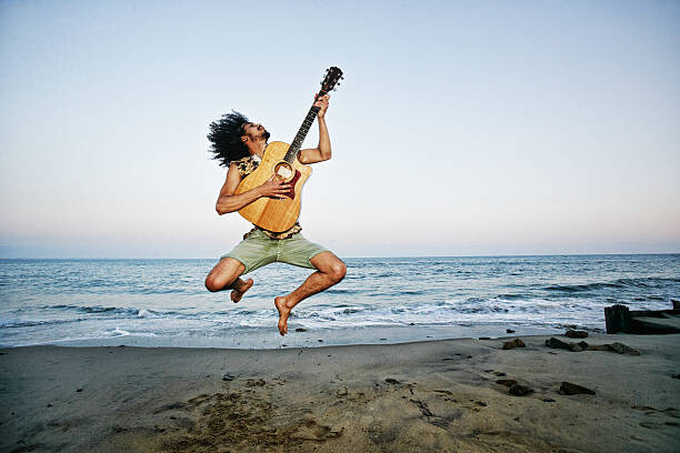 Poster Mixed Race man playing guitar and jumping at beach