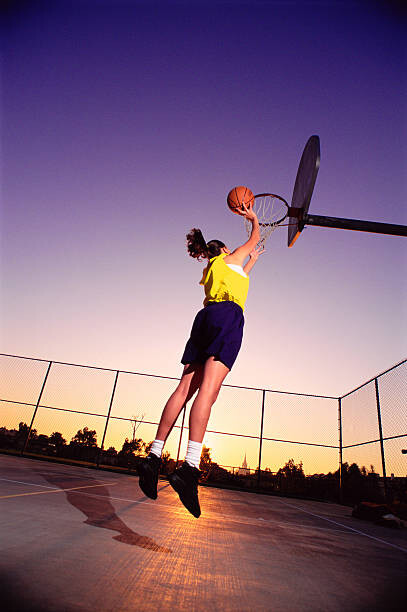 Poster Young woman dunking basketball in net,