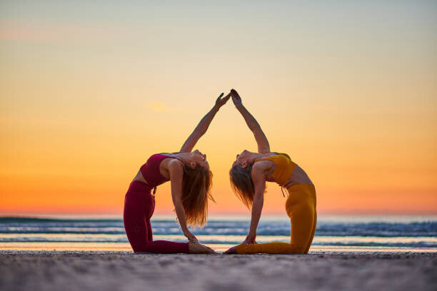 Плакат Two women doing yoga on the beach at sunrise